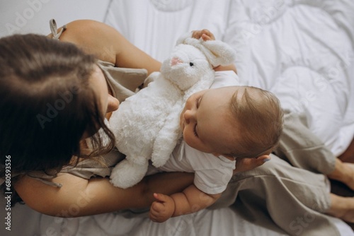 mother holding her baby son on hands and her knees and a white rabbit toy fluffy photo