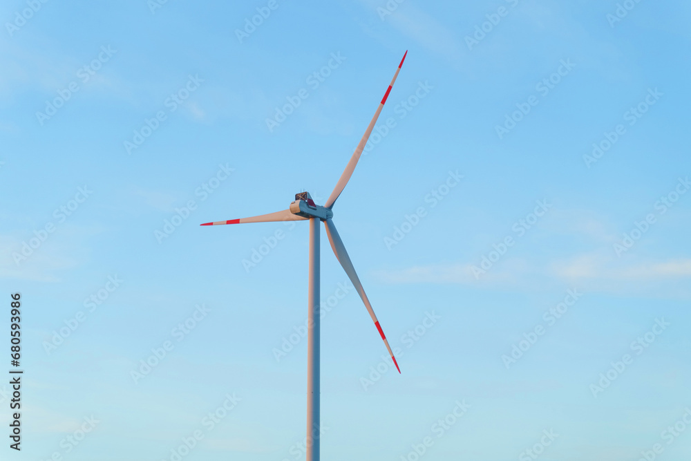 Wind turbine for power generation outdoors with sun and blue sky.