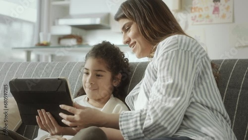 Wallpaper Mural Joyous little girl sitting on sofa and playing online game on digital tablet together with mom while having fun at home Torontodigital.ca