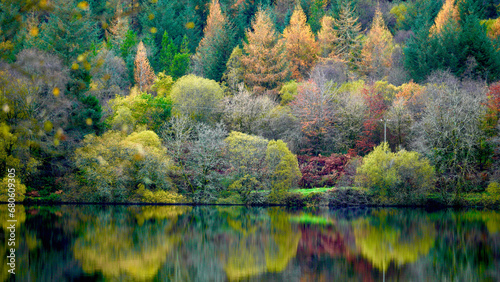 Autumn colours at Llyn Onn reservoir in the Brecon Beacons. The leaves have changed green to orange, gold, red and yellow. The vibrant seasonal hillside colours are mirrored in the water below photo