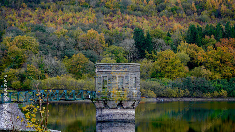 Autumn colours at Tal-y-Bont reservoir in the Brecon Beacons. The leaves have changed green to orange, gold, red and yellow. The vibrant seasonal colours of the hillside reflect in the water below