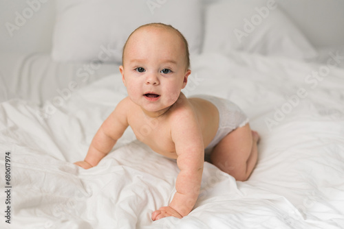 Smiling newborn baby on a white bed at home, the concept of a happy healthy infant baby. Generation alpha and gen alpha