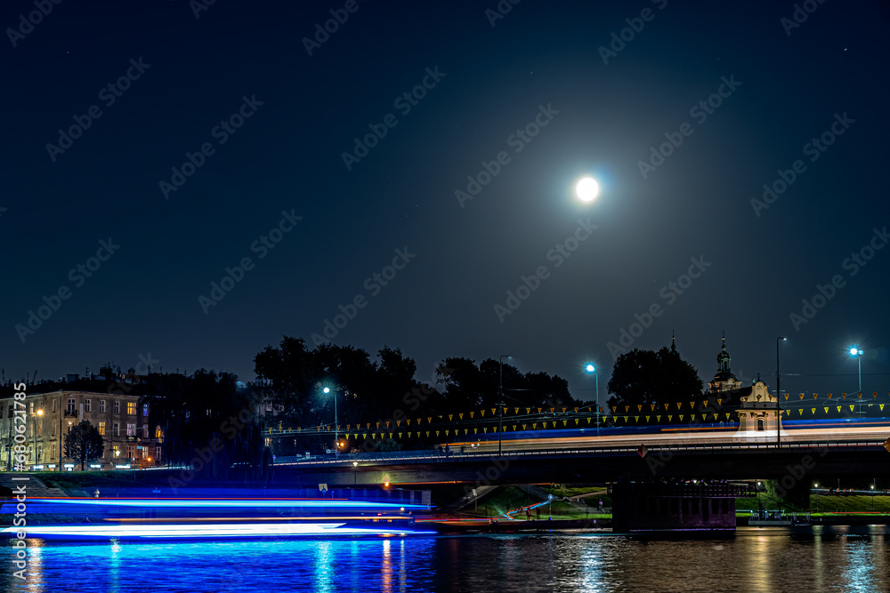 Night lights over the Vistula River in Krakow at the rising of the full moon.