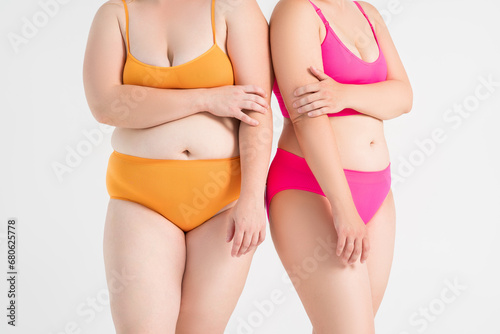 Two overweight women with fat flabby bellies, legs, hands and hips on gray background, plastic surgery and body positive concept photo