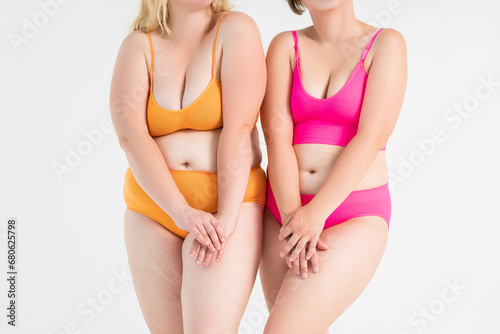 Two overweight women with fat flabby bellies, legs, hands and hips on gray background, plastic surgery and body positive concept photo