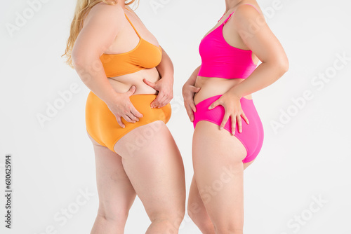 Two overweight women with fat flabby legs, hands, hips and buttocks on gray background, plastic surgery and body positive concept