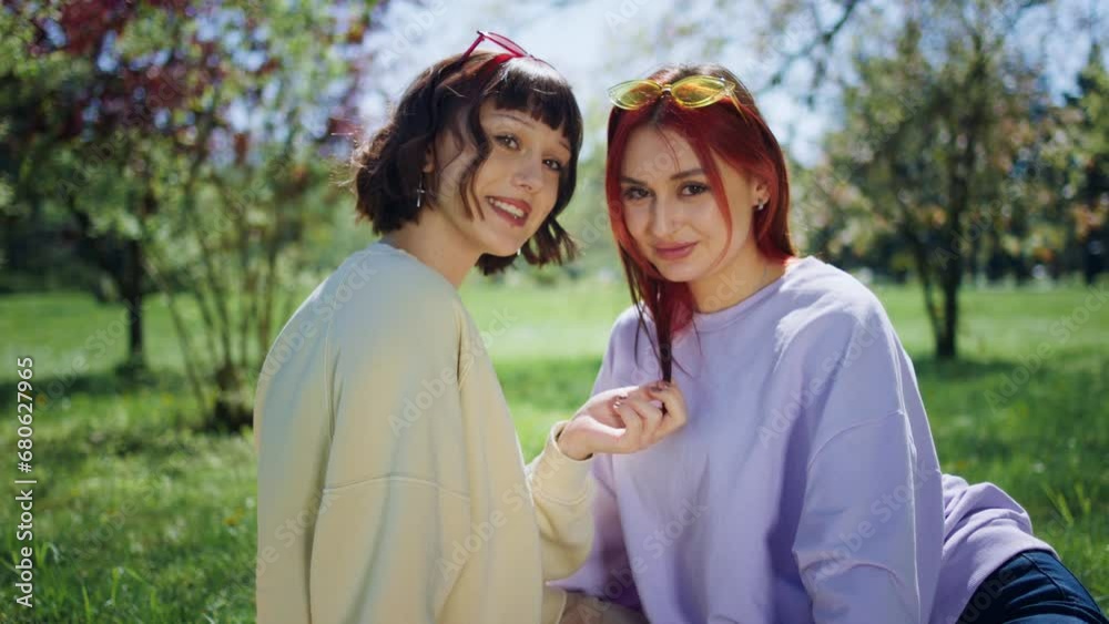 In front of the camera charismatic and Bea ladies posing in front of the camera in the middle of the park they are sitting down on the grass together In front of the camera charismatic and Bea ladies posing in front of the camera in the middle of the park they are sitting down on the grass together