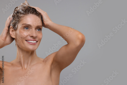 Beautiful happy woman washing hair on light grey background. Space for text