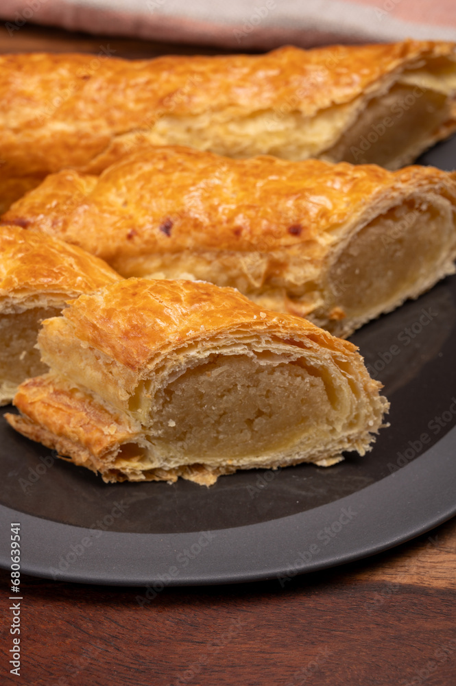 Fresh baked Dutch filled spicy cookies from puff pastry with almonds on black board close up