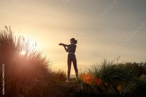 silhoutte of a sporty woman doing an arm stretch exercise at sunrise.