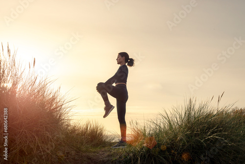 silhoutte of a sporty woman doing a leg stretch exercise at sunrise. photo