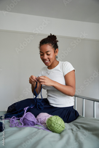 Biracial girl with curls hair sitting on bed and knitting. Concept of gender-neutral and sustainable fashion and self expression