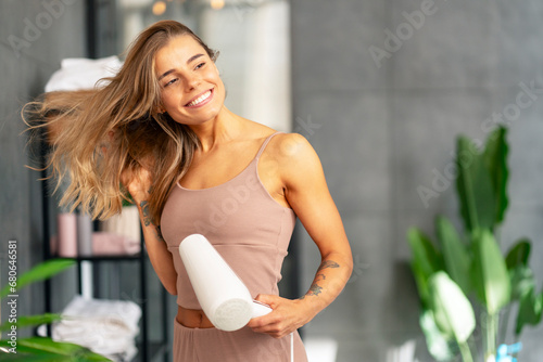 Attractive smiling woman drying hair with hairdryer looking away  standing in modern bathroom, copy space. Natural beauty, morning routine, hair care concept