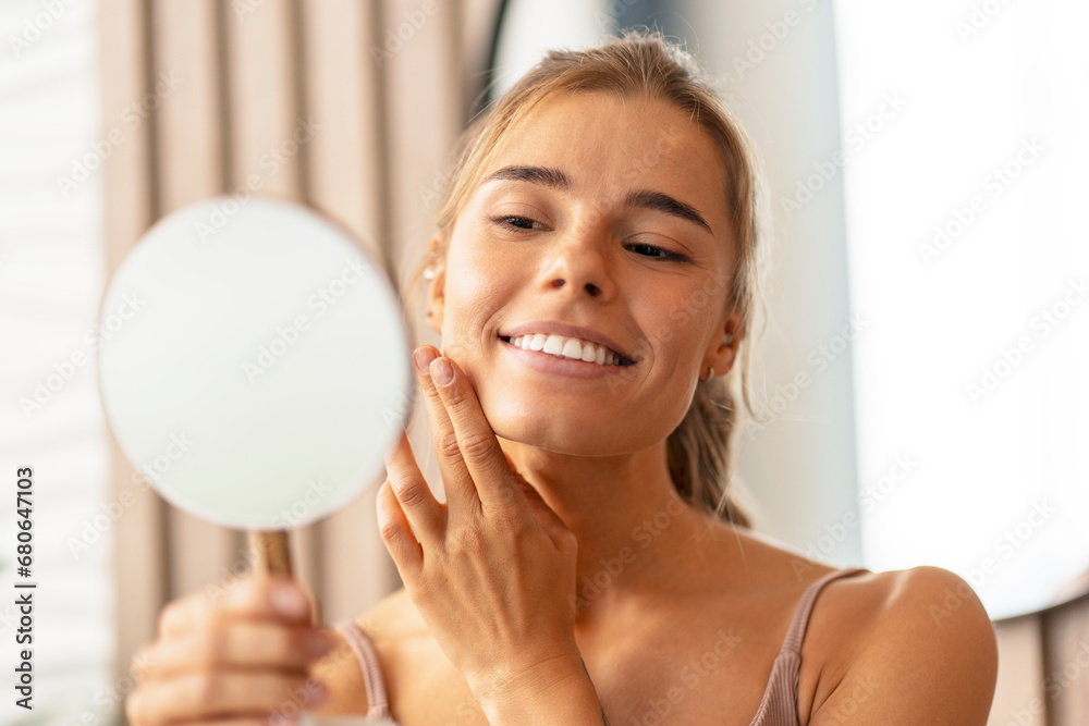 Closeup of attractive smiling woman touching her cheek applying face cream looking in mirror. Makeup, beauty procedure, morning routine concept Closeup of attractive smiling woman touching her cheek applying face cream looking in mirror. Makeup, beauty procedure, morning routine concept