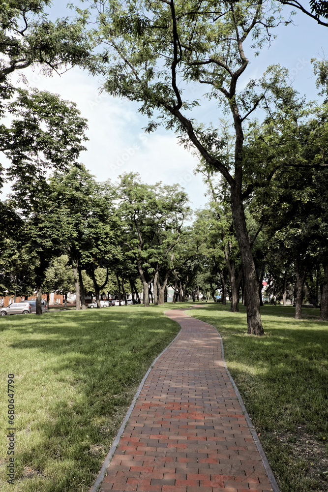 This is a photo of a brick path winding through a park with trees and grass on either side. This is a photo of a brick path winding through a park with trees and grass on either side.