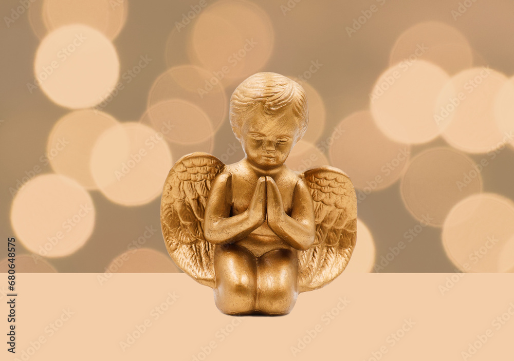 Golden angel figurine in front of a bokeh background. Copy space.