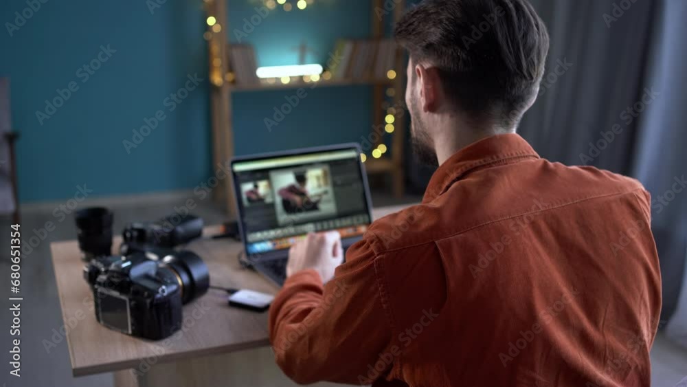 Over the shoulder view of a photographer working at a laptop processing photos in a home office Over the shoulder view of a photographer working at a laptop processing photos in a home office