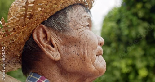 Slow motion scene of Asian farmer who is a rural poor elderly villager standing, holding a hoe, wearing hat, looking at the the sky while he working in the crop field. photo