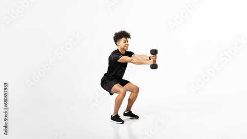 Young sporty guy squatting holding dumbbells over white studio background