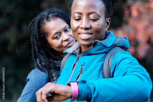 Smiling black mature women monitoring smart watches outdoors in autumn.