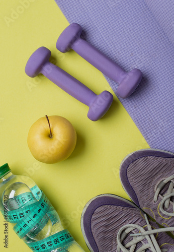 The concept of a healthy lifestyle, fitness, proper nutrition. Sneakers, dumbbells, water and fruits on a bright yellow background.