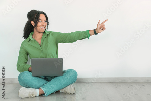 African American woman browsing online with laptop, pointing aside indoor © Prostock-studio