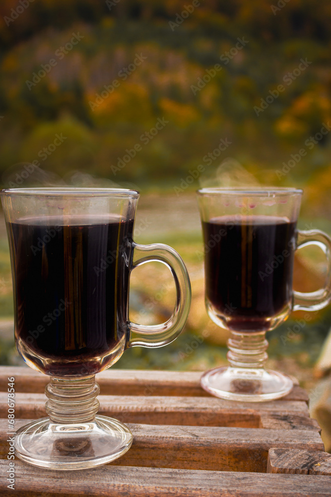 Two glass with mulled red wine on autumn forest background. Picnic with alcohol drinks. Vacations for two. Hot wine at the back yard. Aromatic gluhwein. Autumn travel. Two glass with mulled red wine on autumn forest background. Picnic with alcohol drinks. Vacations for two. Hot wine at the back yard. Aromatic gluhwein. Autumn travel.