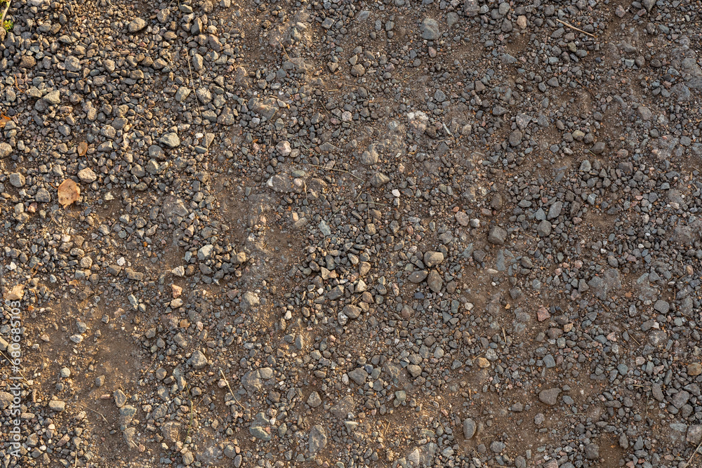 Fototapeta premium Background of small stones in dry earth close-up. Beautiful textured background of pebbles in dry ground. View from above. Concept background of a path made of earth and small cameos.
