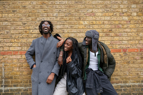Group of three black friends with unique style posing together in front of brick wall 