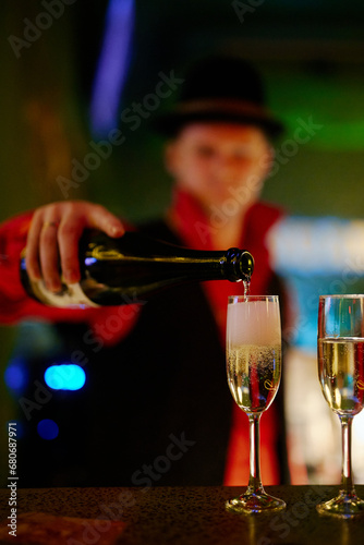 A bartender in a red shirt pours champagne into glasses at night