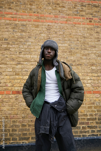 Gen Z black boy with cool winter style posing in front of brick wall