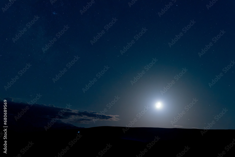 Night starry sky with luminous moon in the mountains. Copy space.