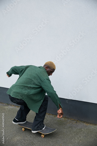 Fashionable black boy with blonde hair riding skateboard on sidewalk