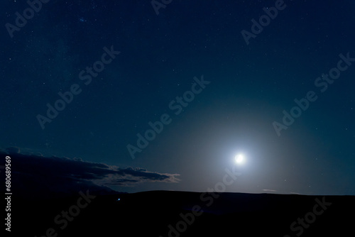 Night starry sky with luminous moon in the mountains. Copy space.