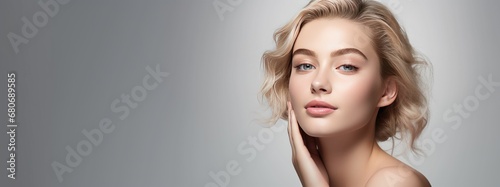 Photograph of a female model with clean and healthy skin touching her face, taken on a studio background.