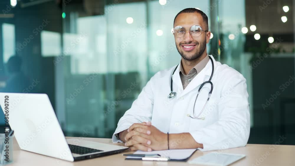 Portrait doctor sitting at desk in office a modern clinic or hospital looking at camera. Black male physician with glasses and stethoscope with glasses Friendly family man therapist or pediatrician Portrait doctor sitting at desk in office a modern clinic or hospital looking at camera. Black male physician with glasses and stethoscope with glasses Friendly family man therapist or pediatrician