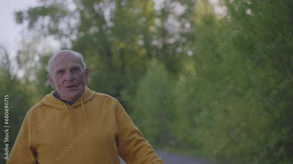 Athletic mature male person runs to goal along path in park at twilight. Joyful pensioner exhales after jogging. Physical activity for health in old age