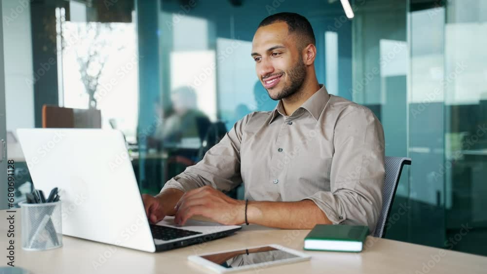 Young businessman working on laptop in modern office lobby space. Arab business man professional learn using computer remote studying, watching online webinar, virtual training from office. Indoor