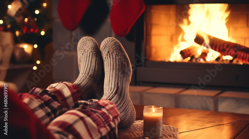 Feet in woolen socks by the holiday fireplace. A couple sits under a blanket, relaxing by the warm fire and warming their feet in woolen socks. The concept of winter holidays and Christmas