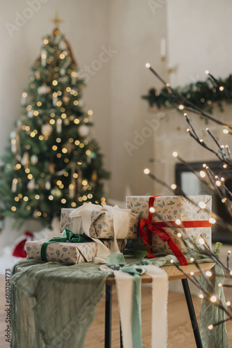 Merry Christmas and Happy Holidays! Stylish wrapped christmas gifts with ribbon on table on background of decorated christmas tree with vintage baubles, rustic fireplace and festive lights