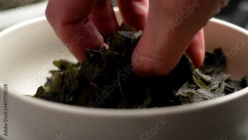 Chef hand taking raw dried Kombu seaweed from a ceramic bowl. Dehydrated asian sea ingredient close up photo