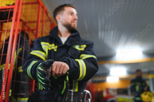Fireman putting on protective uniform and preparing for action while standing in fire station © Serhii