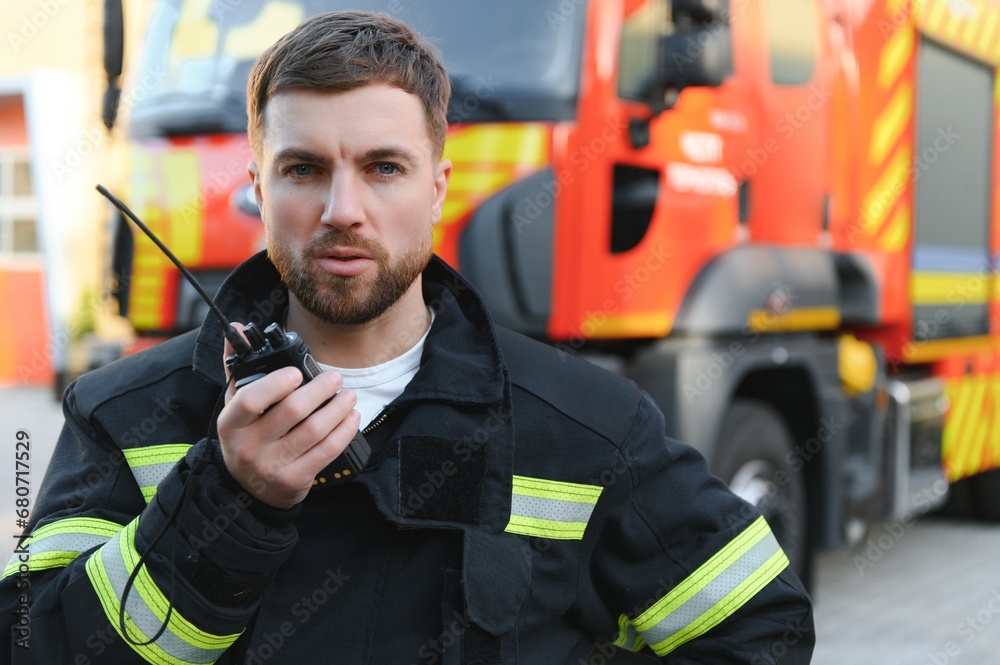 Firefighter in uniform using portable radio set near fire truck outdoors