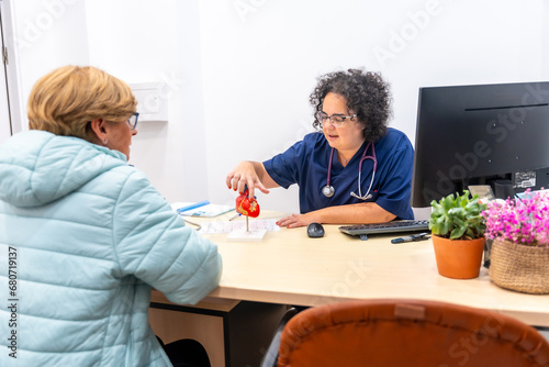 Cardiologist and woman talking in the clinic office with a computer and a hear shape model on the table