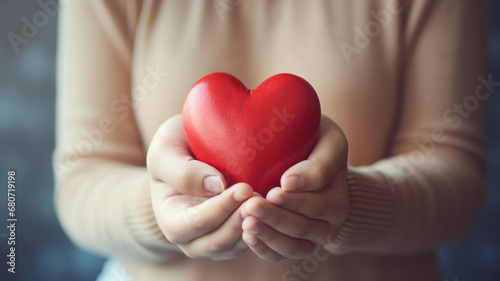 close up of woman  s hands holding red heart with blurred bokeh background. love and health care concept