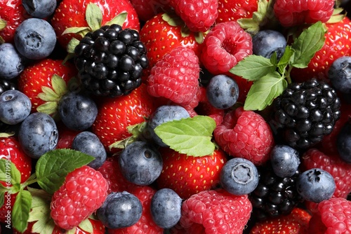 Assortment of fresh ripe berries with green leaves as background  top view