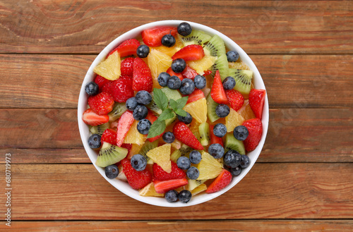 Delicious fresh fruit salad in bowl on wooden table, top view