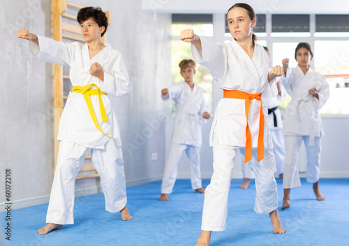 Group of preteen children in kimono trying new martial moves at karate class