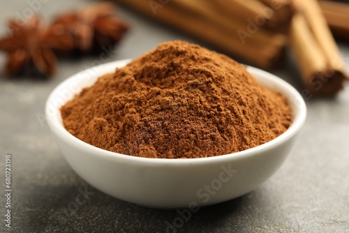 Bowl of cinnamon powder on grey table, closeup
