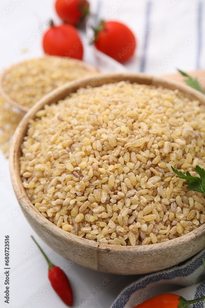 Raw bulgur in bowl and peppers on table, closeup Raw bulgur in bowl and peppers on table, closeup